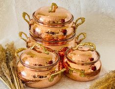 a stack of copper pots sitting on top of a table next to dried grass and stalks