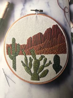 a hand embroidered desert scene with cacti and mountains in the background on a marble surface