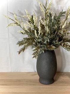 a vase filled with lots of green and white flowers on top of a wooden table