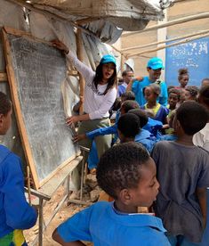 a woman teaching children how to write on a chalkboard