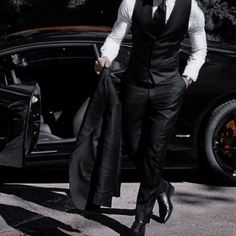 a man in a suit and tie walking towards a black car with his coat open