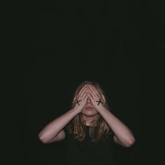 a woman covering her eyes with both hands in front of her face, against a black background