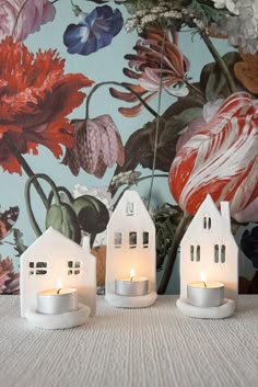 two small white houses sitting on top of a table next to each other with candles in front of them