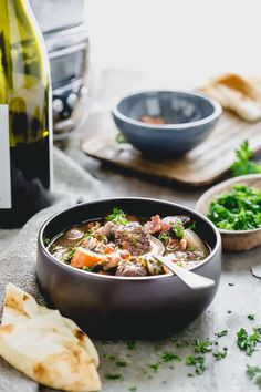 a bowl of soup next to a bottle of wine and some bread on a table