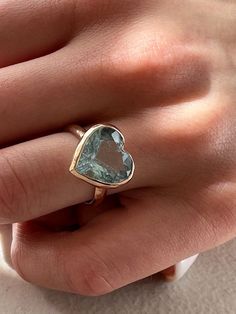 a woman's hand wearing a gold ring with a heart shaped aqua blue topazte