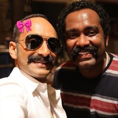 two men are posing for the camera with sunglasses on their heads and one has a pink bow in his hair