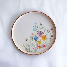 a plate with flowers painted on it sitting on a white tableclothed surface in the shape of a circle