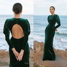 a woman in a green dress standing on the rocks by the ocean with her back to the camera