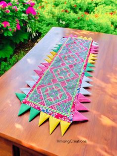 a wooden table topped with an intricately designed rug on it's side and flowers in the background