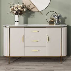 a white and gold sideboard with flowers on it in front of a round mirror