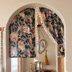 an arched window with floral curtains and decorative objects on the shelf in front of it