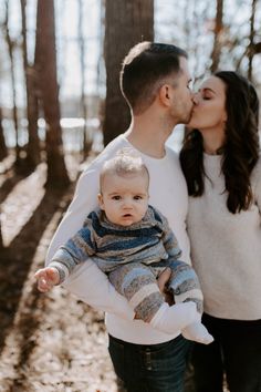 a man and woman holding a baby in the woods