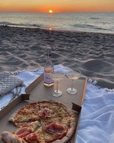 a pizza sitting on top of a beach next to a bottle of wine and two glasses