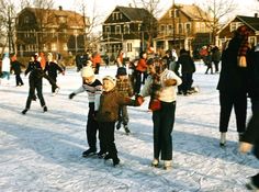 many people are skating on the snow in front of some houses and buildings, one person is holding his hand out to someone else