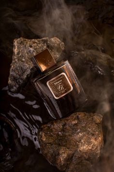 a bottle of perfume sitting on top of a rock in the water next to some rocks