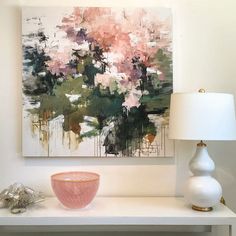 a painting is hanging on the wall above a table with a bowl and lamp next to it