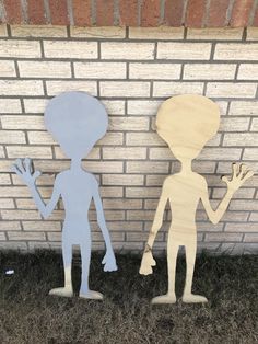 two paper cut out figures standing next to a brick wall