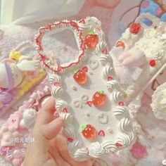 a hand holding a cell phone case made out of white frosted cake and cherries