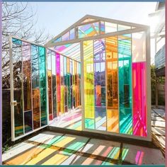 a colorful glass house sitting in the middle of a yard with sun shining through it