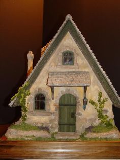 a small house with a green door and window on top of a shelf next to a wall