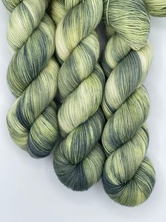 two skeins of green and white yarn on a white surface with one skein in the foreground