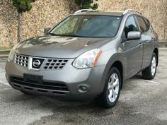 a silver nissan suv parked in a parking lot next to a wall with trees on it