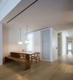 an empty room with a wooden table and bench in the center, along with white walls