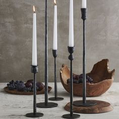 four candles are standing in front of some grapes and plums on a wooden plate