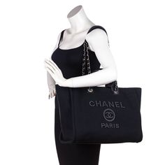 This Chanel Large Deauville Tote is the perfect elevated casual design from Chanel's spring/summer 2020 bag collection. A thick black canvas exterior, referred to as 'mixed fibers' by Chanel, makes up the exterior of this pristine bag, accented by black leather trim and silver-tone hardware. Front and center, the Chanel lettering and logo present in a black faux pearl design, drawing in attention with a hint of shine. Carry this Chanel tote with the dual rolled leather top handles, or wear it on your shoulder with the interwoven leather & chain shoulder straps with a leather comfort guard. The top of this 'it bag' secures via one magnetic snap closure, leading into the black canvas interior. A spacious design, inside you will find one zip pocket along the back wall, two slip pockets, two o Elevated Casual, Chanel Tote, Chanel Spring, Shopping Chanel, Bag Collection, Pearl Design, Casual Design, Design Drawing, Chanel Black