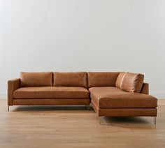 a brown leather couch sitting on top of a hard wood floor next to a white wall