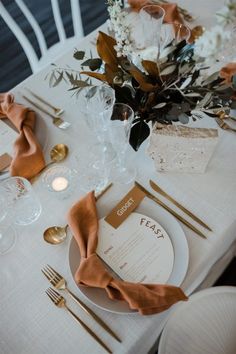 the table is set with white and gold place settings, silverware, napkins, and flowers