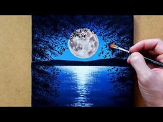 a person holding a paintbrush and painting the moon on a piece of paper with water