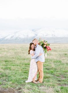 a man and woman standing in an open field with mountains in the background at their wedding