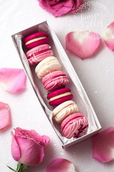 a box filled with pink and white macaroons next to rose petals on a table