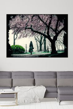 a woman is walking down the street with pink flowers on trees in front of her