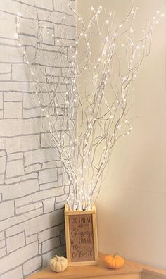 a wooden table topped with a vase filled with white branches and small pumpkins next to a brick wall