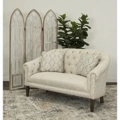 a white couch sitting next to a plant on top of a carpeted room floor