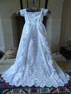 a white dress hanging on a rack in front of a fire place with a rug underneath it