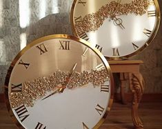 two gold clocks with roman numerals on the faces and numbers are sitting next to each other