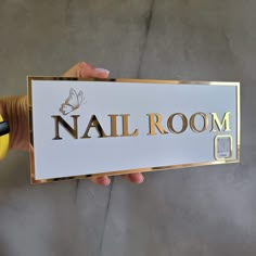 a person holding up a sign that says nail room in gold and black lettering on it