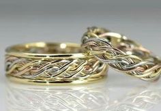 two gold wedding rings sitting on top of each other, one with an intricate design