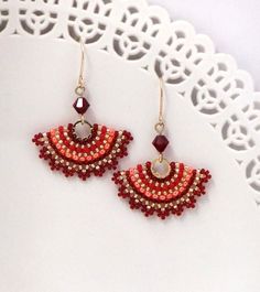 a pair of red and orange beaded earrings on a doily lace tablecloth