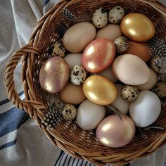 a basket filled with different colored eggs on top of a table next to a blue and white towel