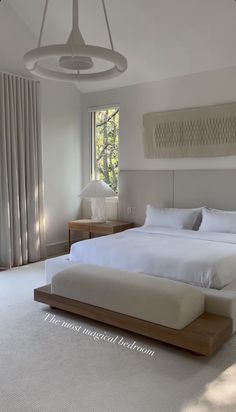 a large white bed sitting in a bedroom next to a window with drapes on the windowsill