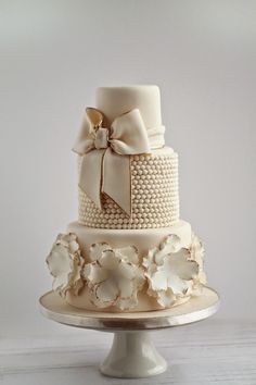 a three tiered wedding cake with white flowers and pearls on the bottom, topped with a bow