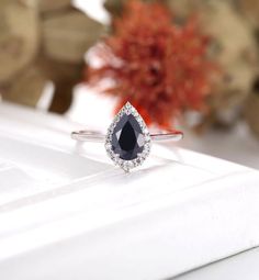 an engagement ring with a pear shaped black diamond surrounded by small white diamonds on a table