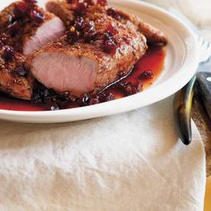 a white plate topped with meat covered in cranberry sauce next to a fork