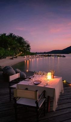 a dinner table set up on a dock with candles and wine glasses in front of it