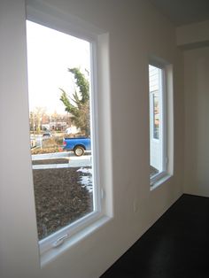 two windows in a white room with a blue car parked on the street behind them