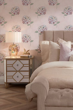 a bedroom with pink flowers on the wall and white bedding, along with an upholstered headboard